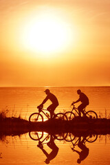 Obraz na płótnie Canvas silhouette of 2 two person - man and woman. Side view of couple riding on seashore with their bicycles. sunset sky on background. couple fallen in love.