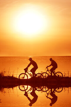 silhouette of 2 two person - man and woman. Side view of couple riding on seashore with their bicycles. sunset sky on background. couple fallen in love.