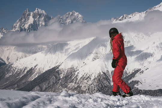 female Snowboarder riding with snowboard in beautiful mountains landscape with clouds and peaks