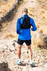 Fototapeta premium Young man practising trail running in the high mountains, while descending down the mountainside
