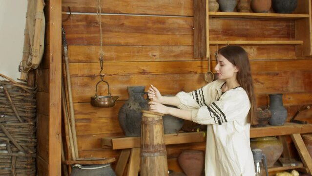 A young woman is churning butter with a wooden churn. An old house