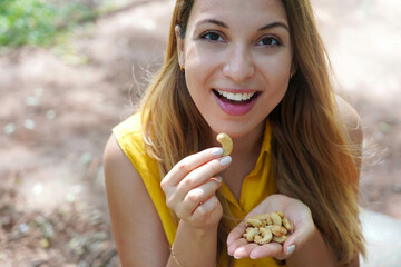 Beautiful healthy girl eating cashew nuts in the park. Looks st camera.