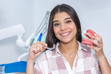 Cheerful ethnic teen girl showing denture and retainer in dental clinic - obrazy, fototapety, plakaty