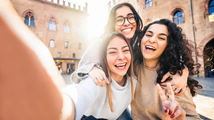 Fotobehang Three young women taking selfie picture with smart mobile phone on city street - Happy beautiful female friends smiling at camera outdoors -  Life style concept with cheerful girls enjoying vacation  © Davide Angelini