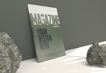 Magazine Mockup on a Clean Army Green Wall With Leafs Shadows and Rocks on the Floor