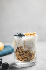 Granola cereal oatmeal with white yogurt, blueberries in a glass on a grey background