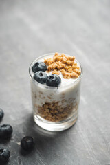 Granola cereal oatmeal with white yogurt, blueberries in a glass on a grey background