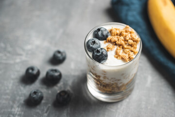 Granola cereal oatmeal with white yogurt, blueberries in a glass on a grey background