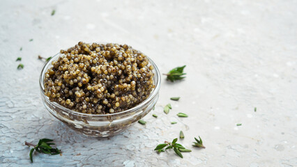 Black sturgeon caviar in a glass bowl. Macro photo. On a gray concrete background. Side view.