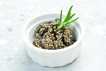 Caviar. Black sturgeon caviar in a bowl. Macro photo. On a gray concrete photo.