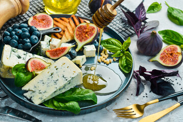 Traditional blue cheese, figs, blueberries and honey in a plate. On a concrete background. Side view.