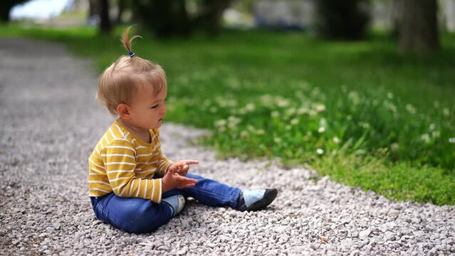 Little girl sits on a gravel path in the garden and wiggles her fingers