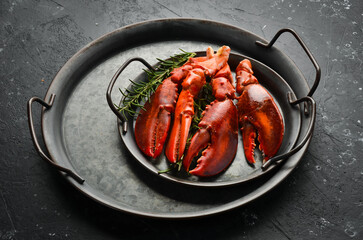 Boiled lobster claws with spices and herbs on a metal plate. On a black stone background.