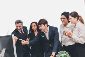 A team of exclusive diversity businesspeople are gathered together in an office, excitedly watching their accomplishment on a laptop computer. Idea for fostering strong teamwork in the workplace.