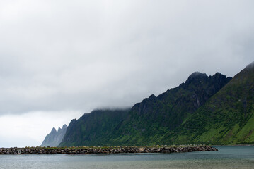 Beautiful nature landscape in North. Scenic outdoors view. Ocean with waves and mountains. Big dark stones. Dramatic storm clouds. Extreme weather, rain and wind. Explore Norway, summer adventure
