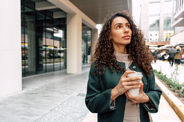 Young and cheerful woman walking with coffee cup through the city