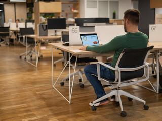 Caucasian bearded man working on laptop in modern coworking space. 