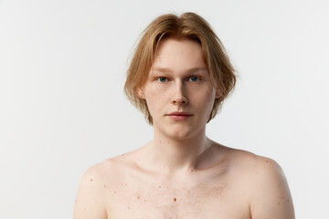 Portrait of young redhead man posing shirtless, looking attentively in camera over grey studio background. Concept of men's health, body and skin care, hygiene and male cosmetology