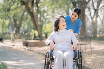 Smiling physiotherapist taking care of the happy senior patient in wheelchair, outdoor.