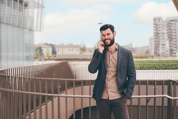 Young contemporary bearded modern businessman outdoors smiling happy talking smartphone having conversation