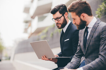 two businessman sitting outdoors business district using sharing netbook computer