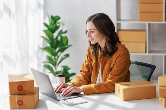 Concept of parcel delivery and selling online, Female seller or retailer Using laptop to check sales of the day on online store to be packed into the parcel and ready to deliver to the customer