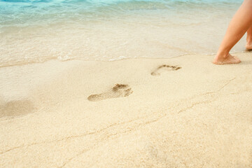 A Beach travel - woman relaxing walking on a sandy beach leaving footprints in the sand. Close up detail of female feet on golden sand at a beach in Greece. Background.