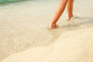 A Beach travel - woman relaxing walking on a sandy beach leaving footprints in the sand. Close up detail of female feet on golden sand at a beach in Greece. Background.