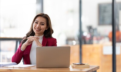 Young businesswoman working at her laptop and going over paperwork while sitting at a desk in an office