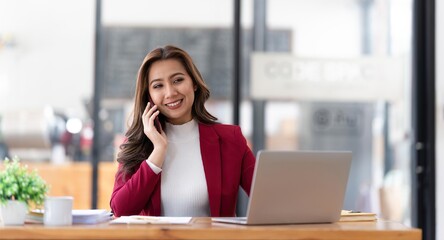 Smiling beautiful Asian businesswoman analyzing chart and graph showing changes on the market and holding smartphone at office