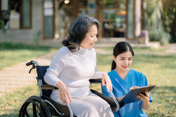 Fototapeta na wymiar Young nurse offering handicapped elderly woman in wheelchair to sign insurance contract at retirement home.
