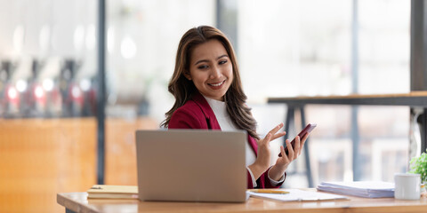 Happy businesswoman using mobile phone while working at office with laptop