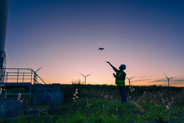 Fototapeta na wymiar asian female engineer using drone for inspection wind turbine farm in evening.