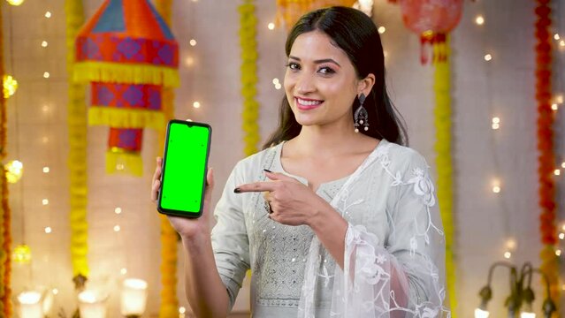 Happy young girl showing green screen mobile phone by pointing finger by looking camera - concept of festival offers, sales and app or application promotion.