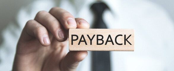 Human hand showing Payback word on wooden block.