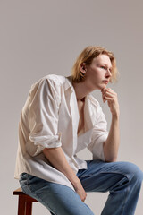 Looking thoughtful. Portrait of young redhead man posing in white shirt and jeans over grey studio background. Concept of men's health, body and skin care, hygiene and male cosmetology