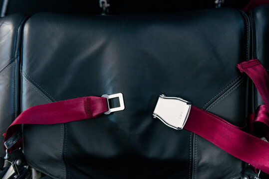 Red seat belt in airplane on black seat. Unlocked. Safety, prevention accident.