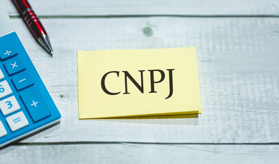 A sigla CNPJ de Cadastro Nacional da Pessoa Jurídica em Português do Brasil escrita em um pedaço de papel que está sobre uma mesa de madeira. Economia brasileira.
 - obrazy, fototapety, plakaty