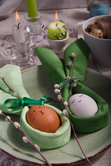Festive Easter table setting with green napkin Easter Bunny, willow tree branches and easter eggs on green plate.