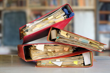 stack of dusty messy file folders with narrow depth of field, blurred office in the back,red tape,...