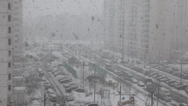 Heavy snowfall in the city (February). Top view from the window on multistorey buildings, street, playground and the yard. Parked cars in the courtyard, children play on the playground.
