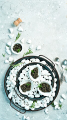 Black caviar in a bowl on chilled white stones. On a gray concrete photo. Top view.
