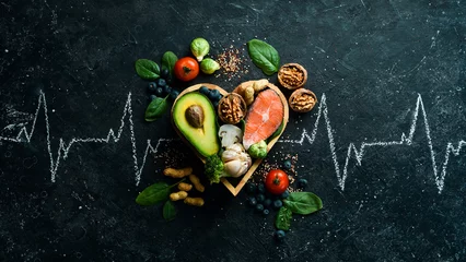 Photo sur Aluminium brossé Manger Food banner. Healthy foods low in carbohydrates. Food for heart health: salmon, avocados, blueberries, broccoli, nuts and mushrooms. On a black stone background. Top view.