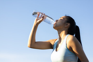 Thirsty Asian female athlete drinking water after exercising outdoors in park.