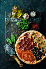 Homemade pizza with sausages, mushrooms, olives and tomatoes. Takeaway food. Home delivery of food. On a black stone background.