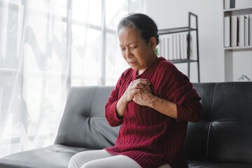 Elderly asian housewife woman sitting on sofa. Heart disease, chest pain, irregular heartbeat