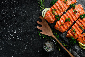 Grilled salmon fillet with spices, lemon and vegetables. On a black background.