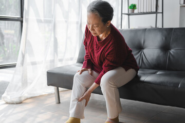 Elderly asian housewife woman sitting on sofa. calf pain © Phushutter