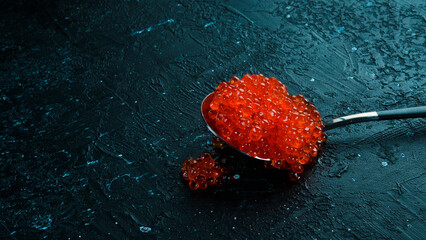 A spoonful of red caviar. Luxury food. On a black background. Free space for text.