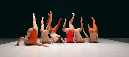 Legs up. Group of young girls, experimantal dancers performing on stage in bodysuits. Creative and...